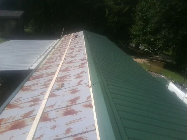 Old rusted panels beside newly installed green metal roofing — Wind Damage Roof Repair by Roofing Brothers in Stillwater
