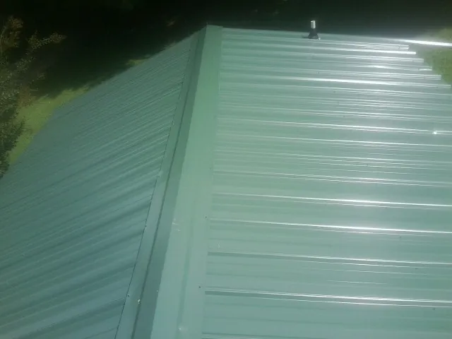 New green metal panels meeting at the ridge of a roof — Flat Roof Repair work by our crew in Stillwater