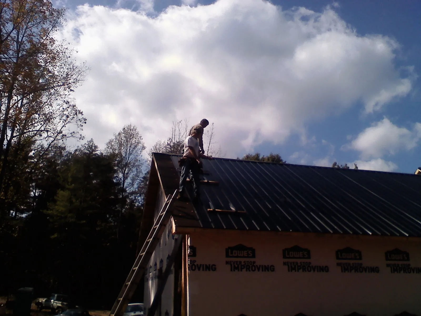 Roofer fastening dark metal panels high against a cloudy sky, from a Roof Inspection job in Stillwater